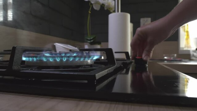 Woman's hand ignites kitchen blue gas in a private house. Gas burner flamer in home