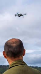 Imagen de un hombre calvo de espalda pilotando un dron y mirando el cielo nublado
