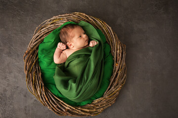 A newborn in a green cloth in a wicker basket
