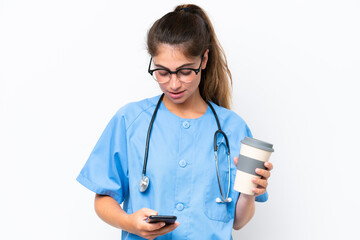 Young nurse doctor woman isolated on white background holding coffee to take away and a mobile