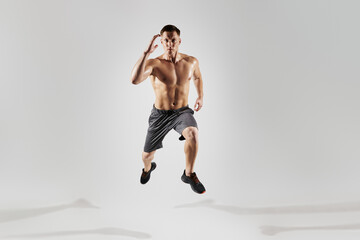 Concentrated muscular man with perfect body running against white background