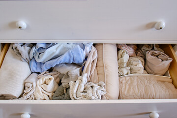 Fototapeta na wymiar Storage of mess children s clothes in a drawer of a white chest, open closet shelf close-up with clutter clothes