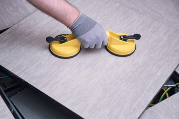 Worker hands with vacuum suction cups for lifting floor panels. A man lifts a floor panel, close-up.