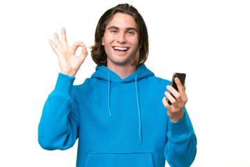 Young handsome man isolated on green chroma background using mobile phone and doing OK sign