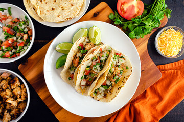 Chicken Tacos Topped with Pico de Gallo and Cheese: Three tacos on a plate surrounded with toppings and tortillas
