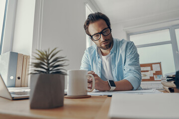 Handsome young man looking thoughtful while sitting at his working place in office