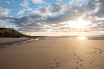 Sandy beach at the sea under a sky painted with clouds and a golden sun, showing an Amazing colorful sunset. Picturesque nature scenery.Clouds reflected in water. Zen-like tranquil atmosphere no