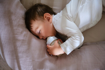 Toddler baby sleeps with a nipple from a bottle of milk formula in his mouth. The child sleeps at...