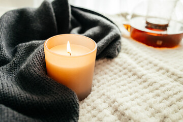 Autumn decor. A burning candle next to a knitted woolen sweater and a pot of hot tea. Atmospheric,...