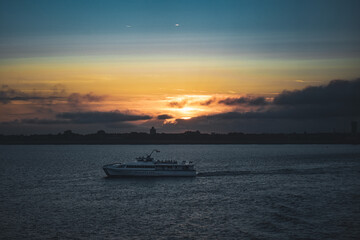 sailboat against Orange red blue sunset sunrise with blue ocean sea land port harbour