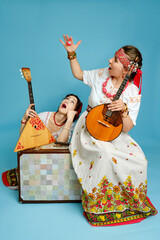 Women musicians in Russian folk dresses with musical instruments on a blue studio background. Happy...