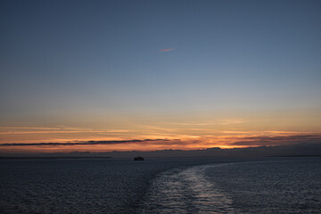 Boat trails in blue ocean sea and orange yellow blue sunset sunrise 