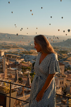 Tourist girl standing and looking to hot air balloons in Cappadocia, Turkey. Happy Travel in Turkey concept. Woman on a mountain top enjoying wonderful view. High quality photo
