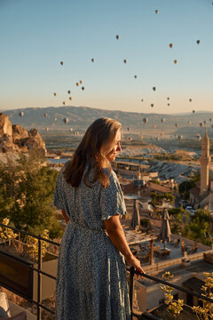Tourist girl standing and looking to hot air balloons in Cappadocia, Turkey. Happy Travel in Turkey concept. Woman on a mountain top enjoying wonderful view. High quality photo
