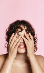 Vertical shot of curly girl washes her face, using cleansing gel treatment from blemishes, better skin tone and no acne, pink background