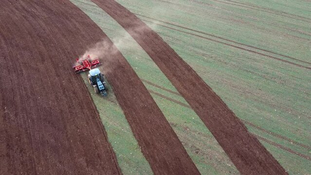 Aerial view of blue tractor plowing the field and exits the frame. Tractor disk harrow on a ploughing soil. Farmer with tractor disking a field in sowing season.