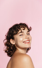 Skin care. Woman with beauty face and healthy facial skin portrait. Beautiful curly girl model with natural makeup touching glowing hydrated skin on pink background closeup. High quality image - obrazy, fototapety, plakaty