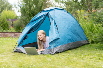 A young girl lying on the grass in the tourist tent with a laptop and working remotely