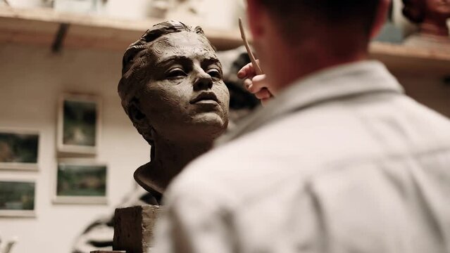 Hands of young artist sculpturing a clay head in the art class. Sculptor creates woman sculpture.
