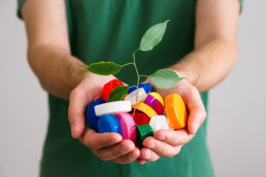 Hands holding a handful of colorful plastic lids with green leaves. Concept of environmental pollution and eco friendly behavior