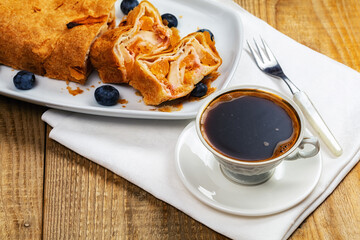 cup of coffee and piece of apple strudel on wooden table.