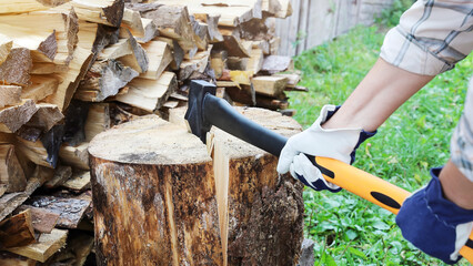 Hands in protective gloves hold axe for cracking firewood, hit for splitting into pieces