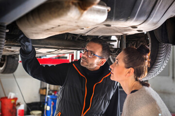 auto mechanic working in car. Car repair. A mechanic and a female driver are looking at the car's chassis. 