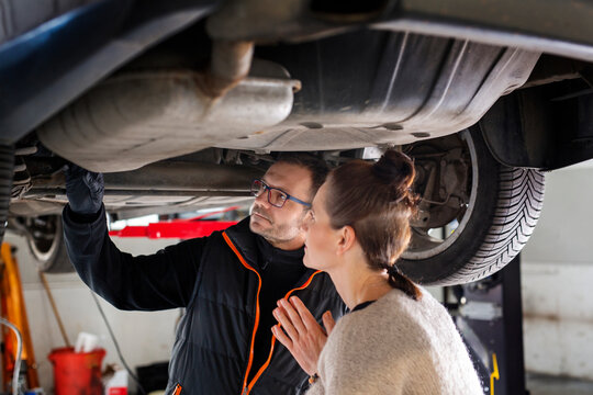 mechanic changing car engine. Car repair. A mechanic and a female driver are looking at the car's chassis. 