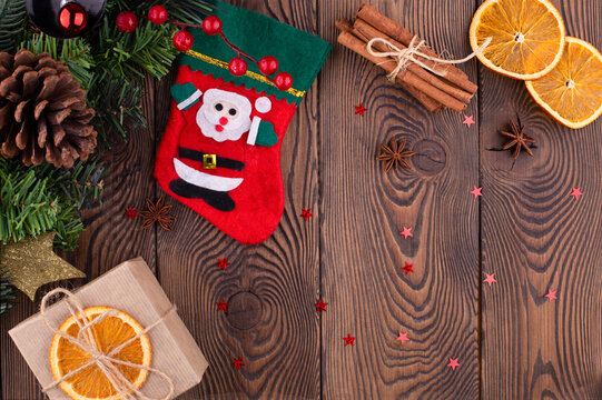 Red felt stocking with the image of Santa Claus, fir branches, cones and Christmas toys, gifts, dried oranges, on a wooden table. Top view, copy space
