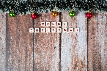 Merry Christmas written with letters of a game and Christmas ornaments on a wooden background