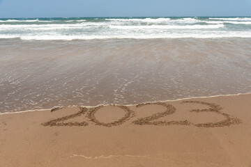 Sea waves entering the number 2023 written in the sand.