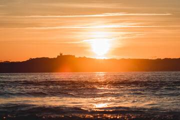 Spectacular panoramic view of a castle on the horizon on the mountain over the sea at sunset during a surf and travel week experience in Somo, Cantabria (Spain)