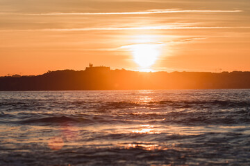 Spectacular panoramic view of a castle on the horizon on the mountain over the sea at sunset during a surf and travel week experience in Somo, Cantabria (Spain)