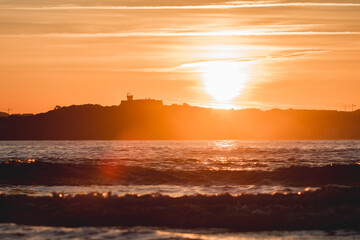 Spectacular panoramic view of a castle on the horizon on the mountain over the sea at sunset during a surf and travel week experience in Somo, Cantabria (Spain)