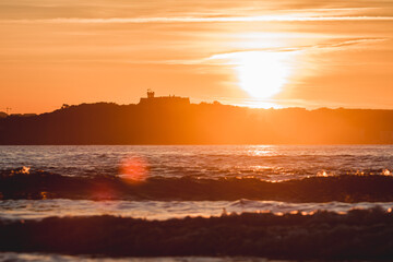 Spectacular panoramic view of a castle on the horizon on the mountain over the sea at sunset during a surf and travel week experience in Somo, Cantabria (Spain)