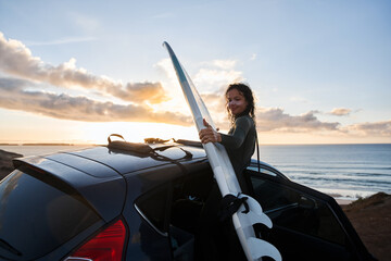 Surfer woman getting ready for surfing vacation and take her surf from the car roof