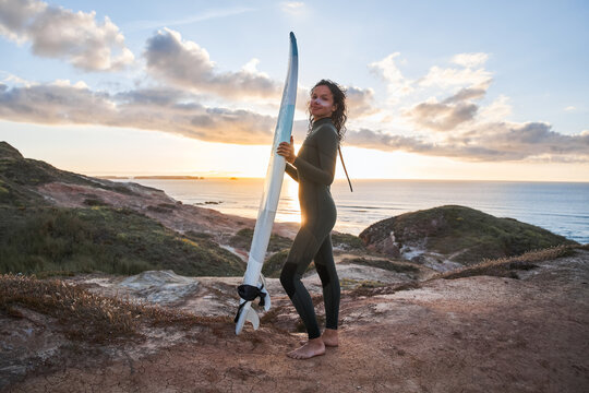 Professional female surfer holding surf board and posing at the hill near the wild ocean beach