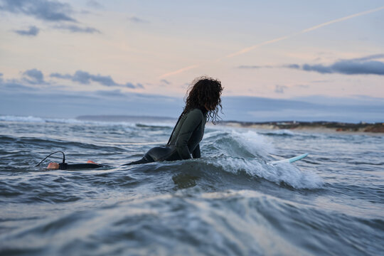Curly woman wearing wetsuit enjoying of the wavy sea with her surfboard during the evening