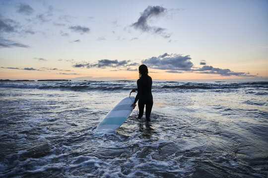 Female surfer entering at the cold ocean water with board and preparing for the training