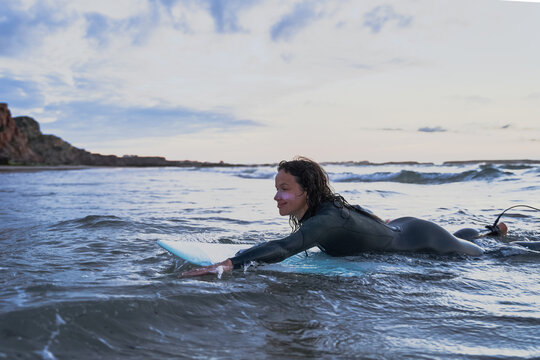 Happy female surfer laying at the board and training during the summer