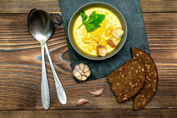 Vegetarian autumn pumpkin traditional soup with seeds, creamy silky texture, cilantro parsley dill greens, croutons, bread, garlic on wooden background. healthy vegan food concept, Top view