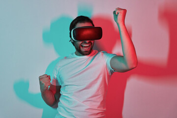 Happy young man in virtual reality eyeglasses gesturing with colorful shadows in the background
