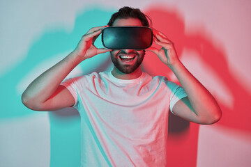 Happy young man adjusting his virtual reality eyeglasses with colorful shadows in the background