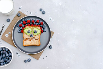 Funny scary monster face smile on halloween sandwich toast bread with peanut butter, blueberry, raspberry on plate,bats on gray background close up. Kids child sweet dessert breakfast lunch food