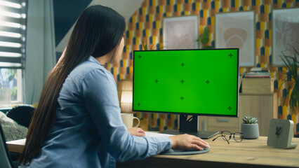 Asian woman sitting at the table and looking at screen of personal computer while surfing the...