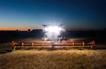 Working combine harvester captured in motion with front headlights illuminating the field at night