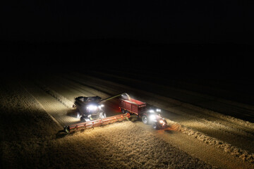 Illuminated field at night during the end of harvesting season: Aerial view of combine harvester...