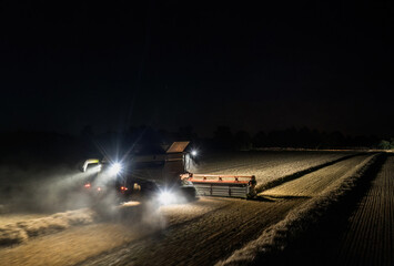Aerial view of combine harvester working at night with lights illuminating the wheat field