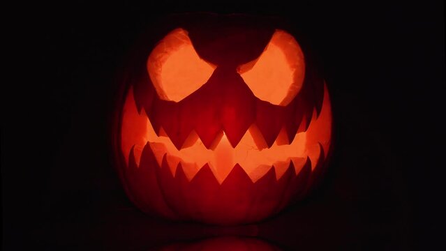 Halloween pumpkin spooky face with candle light on black background. Orange scary Jack O Lantern 4K.