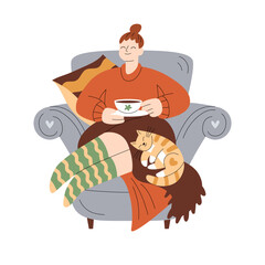 Smiling girl in warm clothes rests in armchair with a cute ginger cat, holds a cup of warm drink